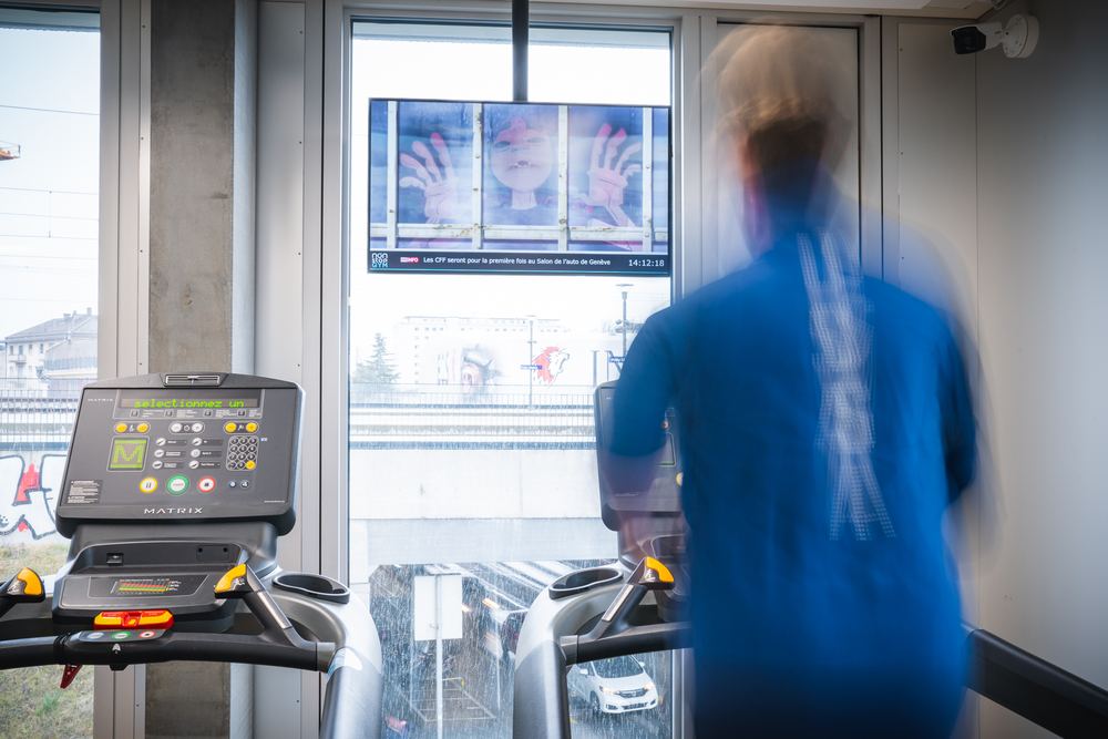 Écran diffusant un bandeau d'informations près des tapis de course, Non-Stop Gym